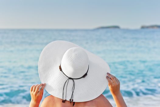 A woman sunbathing on a deck chair on the beach and holding hands hat