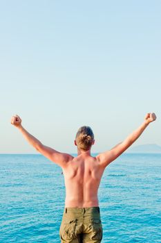 a man with a naked torso is by the sea and put his hands up at dawn