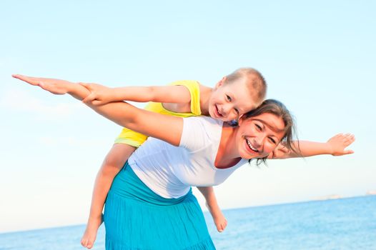 mother and son sitting on her back, happy playing on the beach