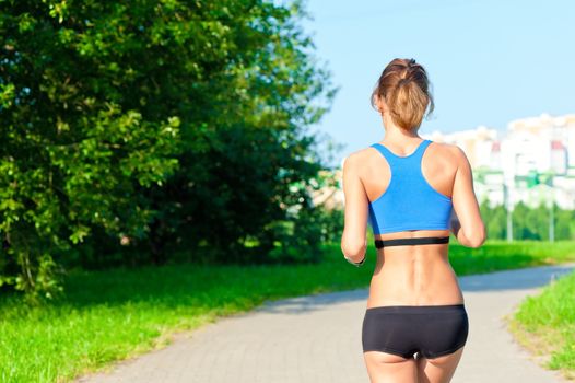 athletic girl in a top and shorts running on the road in the park, not far from the city