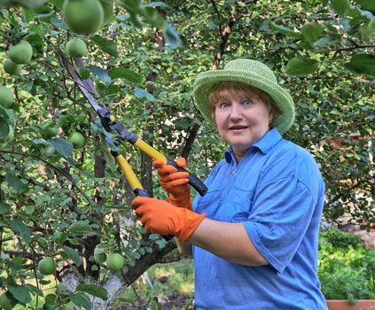 Senior woman holding in hands shears on a background of apple trees
