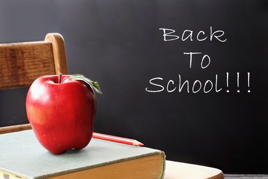 School books with apple sitting on a student desk in front of a chalk board. 
