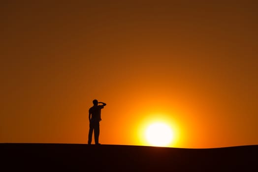 Man silhouette on horizon looks ahead to gold sunset sun on orange and yellow sky