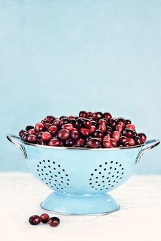 Fresh cranberries in a colander against a blue background.
