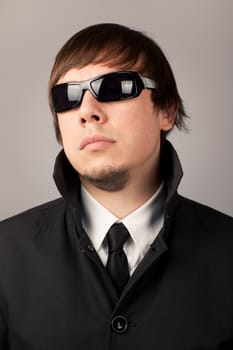 Close-up portrait of serious man in a business suit and sunglasses. On a gray background