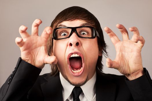 Stilish businessman screaming ang expressing anger. On a grey background