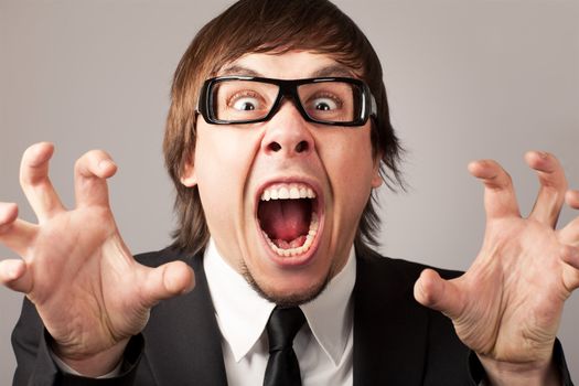 Stilish businessman screaming ang expressing anger. On a grey background