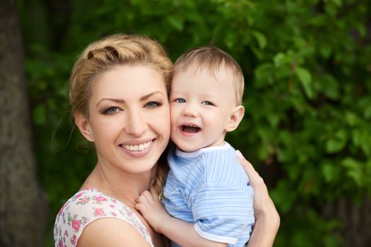 happy blond mom with her little son enjoying nature on a background of green leaves. Much of copyspace