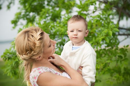 happy blond mom with her little son enjoying nature on a background of green leaves. Much of copyspace