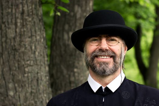 Portrait of a senior businessman smiling, wearing a suit and hat, as well as old fashion eyeglasses. Outdoors.