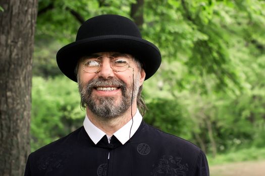Portrait of a retro styled senior, wearing a suit and hat, as well as old fashion eyeglasses. Outdoors.