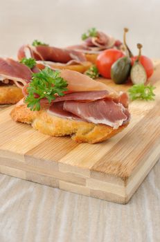 slices of bread with Spanish jamon serrano on a wooden board