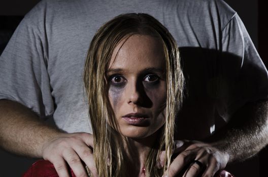 portrait of an abused woman with untidy hair and smudged makeup with a man standing behind her holding his hands on her shoulders cropped horizontally