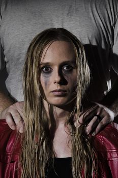 portrait of an abused woman with untidy hair and smudged makeup with a man standing behind her holding his hands on her shoulders cropped vertically