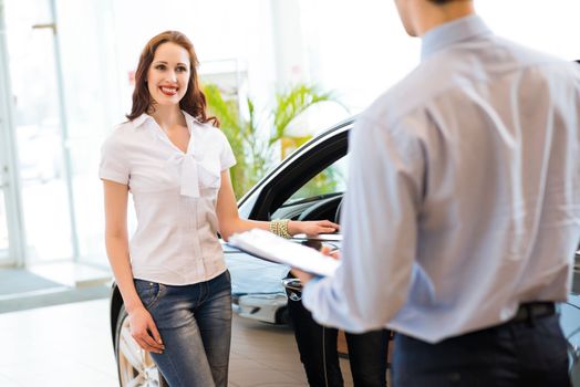 cute woman chooses a new car in the lounge car sales