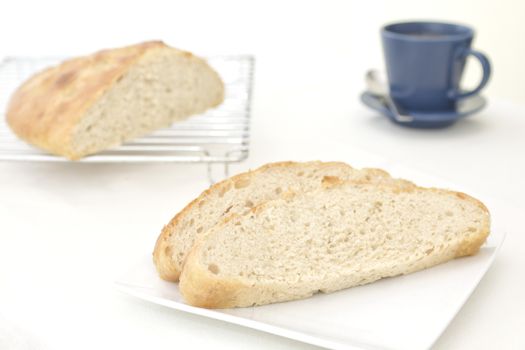 slices of homemade garlic and rosemary focaccia bread on a plate, with the cut loaf on a cooling rack in the background