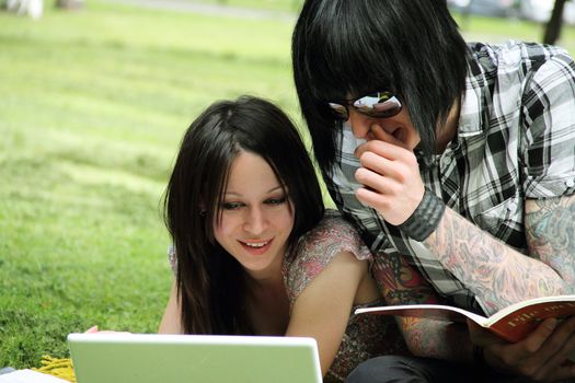 Couple of young students studying outdoors with laptop and books