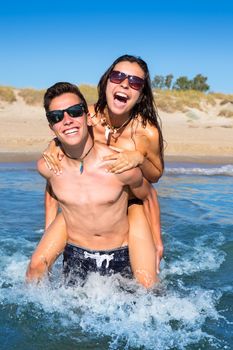 Teen couple enjoying piggyback on summer beach shore splashing water