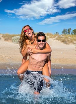 Teen couple enjoying piggyback on summer beach shore splashing water