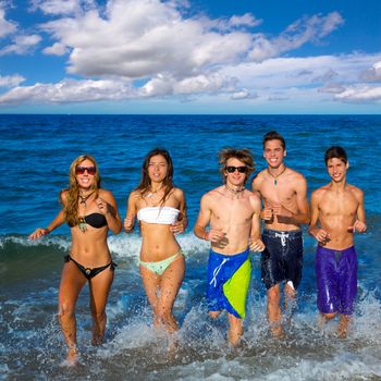 Teenagers group running happy splashing on the beach in summer vacations