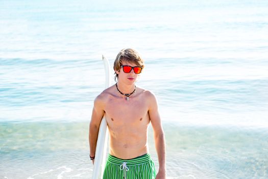 Boy teenager with surfboard on beach shore and orange sunglasses