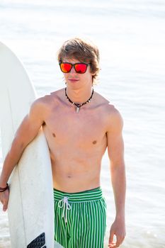 Boy teenager with surfboard on beach shore and orange sunglasses