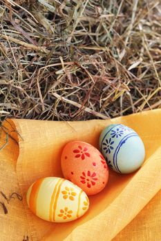 Three colored Easter eggs and orange textile on hay at sunny day