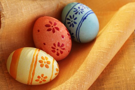 Three colored Easter eggs on orange textile at sunny day