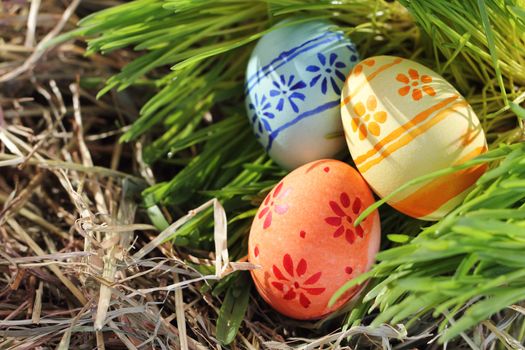 Three colored Easter eggs on hay and green grass renovation concept