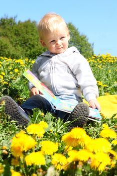 Small child sitting with book on spring flower field