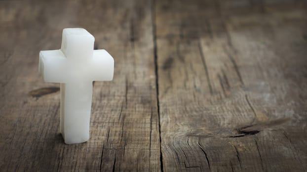 Religious cross out of wax on wooden textured background.