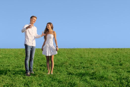 Young couple on summer field discussing something and smiling