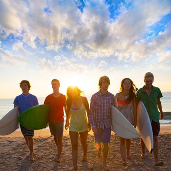 Surfers teen boys and girls group walking on beach at sunshine sunset backlight