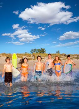 Teen surfers boys and girls group running happy to the beach splashing water