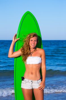 Blond surfer teen girl holding surfboard on blue beach