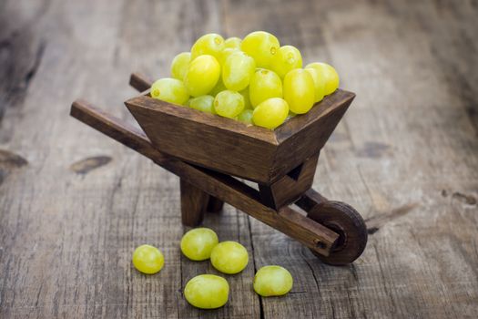 A wheelbarrow full of fresh green grapes on wood background