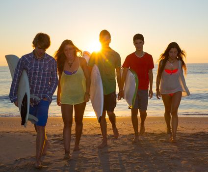 Surfers teen boys and girls group walking on beach at sunshine sunset backlight