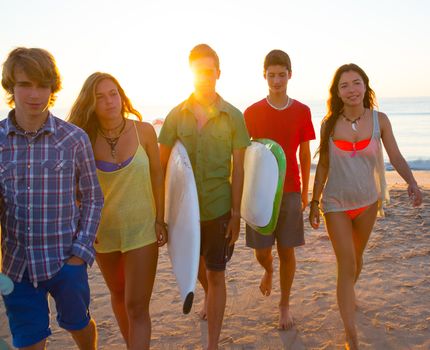 Surfers teen boys and girls group walking on beach at sunshine sunset backlight