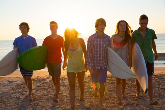 Surfers teen boys and girls group walking on beach at sunshine sunset backlight