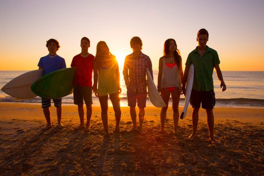 Surfers teen boys and girls group walking on beach at sunshine sunset backlight