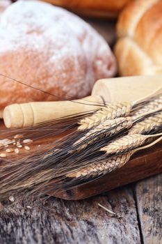 Wheat with variety of freshly baked breads and rolling pin against a rustic background.