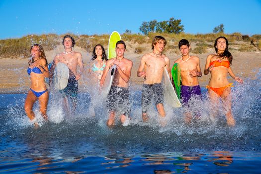 Teen surfers boys and girls group running happy to the beach splashing water