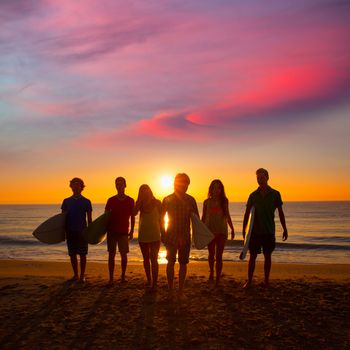 Surfers teen boys and girls group walking on beach at sunshine sunset backlight