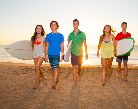 Surfers teen boys and girls group walking on beach at sunshine sunset backlight