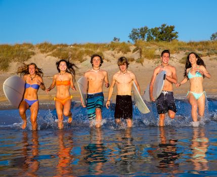 surfer teenagers boys and girls group running happy to the beach splashing water