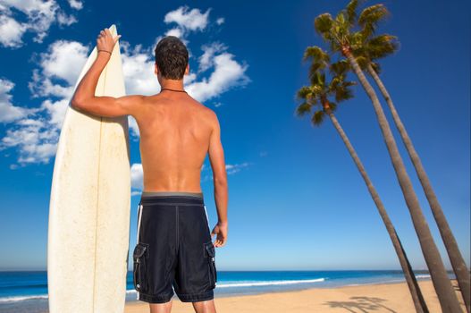 Boy surfer back rear view holding surfboard on California palm trees beach
