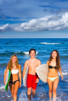 boys and girls teen surfers coming out from the blue beach walking