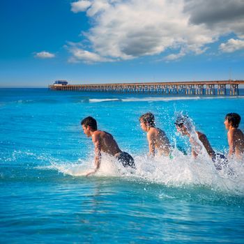 Teenager surfers surfing running jumping on surfboards at Newport pier beach California