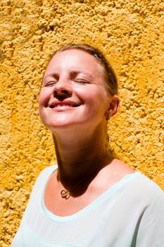 Girl Enjoying the Sun in front of a yellow wall
