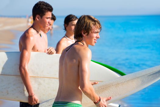 Surfer teen boys talking on beach shore holding surfboards
